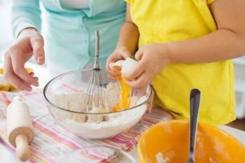 family, cooking, baking and people concept - close up of mother and little daughter breaking egg into bowl and making dough at home kitchen. mother and daughter making dough at home kitchen