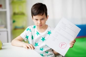 childhood, education and people concept - sad boy holding school test with f grade. sad boy holding school test with f grade