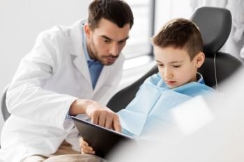 medicine, dentistry and healthcare concept - male dentist showing tablet pc computer to kid patient at dental clinic. dentist showing tablet pc to kid patient at clinic
