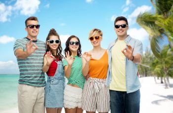 friendship, travel, tourism and summer holidays concept - group of happy smiling friends in sunglasses showing ok hand sign over tropical beach background in french polynesia. friends showing ok over tropical beach background
