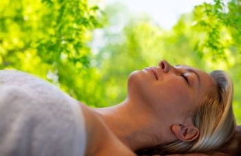 beauty, wellness and relaxation concept - beautiful young woman lying on massage table in spa over green natural background. young woman lying on massage table in spa