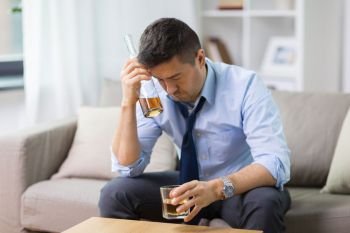 alcoholism, alcohol addiction and people concept - male alcoholic with bottle and glass drinking whiskey at home. alcoholic with bottle drinking whiskey at home