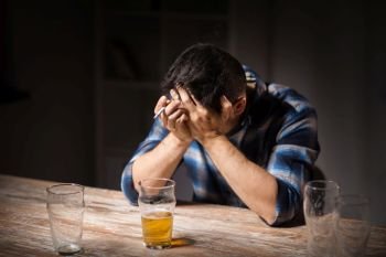 alcoholism, alcohol addiction and people concept - male alcoholic drinking beer and smoking cigarette at night. drunk man drinking alcohol and smoking cigarette