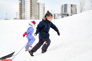 childhood, sledging and season concept - happy little kids with sleds climbing snow hill in winter. kids with sleds climbing snow hill in winter