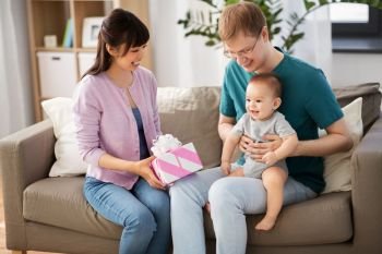 family, parenthood and mothers day concept - happy mother receiving gift box from father and baby boy at home. happy family with gift and baby boy at home