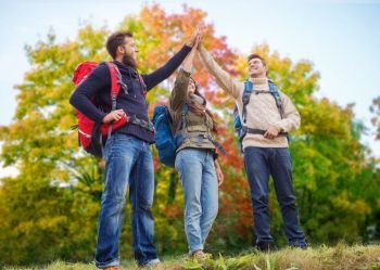 travel, tourism, hike, gesture and people concept - group of smiling friends with backpacks making high five over autumn trees background. friends hiking and making high five in autumn