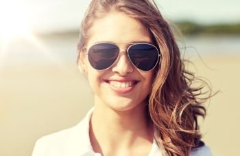 summer vacation, holidays, eyewear and people concept - smiling young woman in sunglasses on beach. smiling young woman in sunglasses on beach