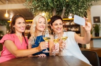 people, technology and lifestyle concept - women drinking wine and taking selfie by smartphone at bar or restaurant. women taking selfie by smartphone at wine bar