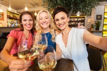 people, technology and lifestyle concept - women drinking wine and taking selfie at bar or restaurant. women taking selfie at wine bar
