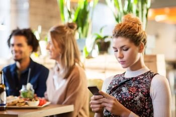 technology, lifestyle and people concept - woman with smartphone and friends at restaurant. woman with smartphone and friends at restaurant