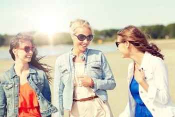 summer vacation, holidays, travel and people concept - group of smiling young female friends in sunglasses and casual clothes walking along beach. group of smiling young female friends on beach