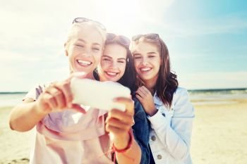 summer vacation, holidays, travel, technology and people concept- group of smiling young women taking sulfide with smartphone on beach. group of smiling women taking selfie on beach
