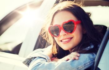summer holidays, valentines day, travel, road trip and people concept - happy teenage girl or young woman heart shaped sunglasses in car. happy teenage girl or young woman in car