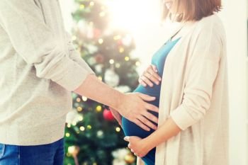 pregnancy, winter holidays and people concept - close up of happy man touching his pregnant wife belly home at christmas. close up of man and pregnant woman at christmas