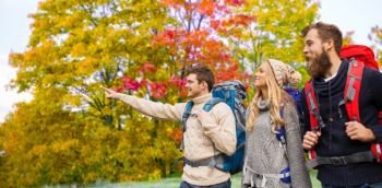 travel, tourism, hike and people concept - group of smiling friends with backpacks hiking over autumn trees background. group of friends with backpacks hiking in autumn