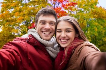 people, leisure and technology concept - happy teenage couple taking selfie over autumn park background. happy couple taking selfie in autumn