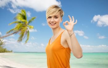 travel, tourism and summer holidays concept - happy smiling young woman over exotic tropical beach with palm trees background showing ok hand sign. happy smiling young woman showing ok hand sign