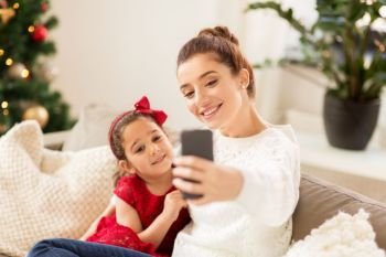 christmas, technology and family concept - happy mother and little daughter taking selfie by smartphone at home. family taking selfie by smartphone at home