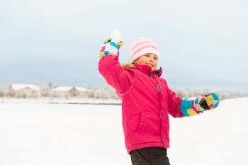 childhood, leisure and season concept - happy little girl throwing snowball in winter. happy girl playing and throwing snowball in winter