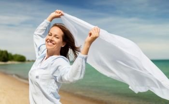 people and leisure concept - happy woman with shawl waving in wind on summer beach. happy woman with shawl waving in wind on beach