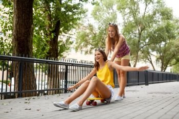 friendship, leisure and people concept - happy teenage girls or friends riding skateboard on city street in summer. teenage girls riding skateboard on city street