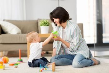 family, child and motherhood concept - happy mother with little baby son playing developmental toys and sippy cup at home. happy mother giving sippy cup to baby son at home