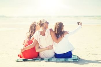 summer vacation, holidays, travel, technology and people concept- group of smiling young women taking selfie with smartphone on beach. happy women taking selfie by smartphone on beach