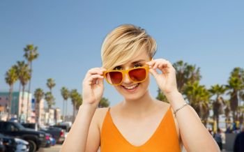 travel, tourism and summer holidays concept - portrait of happy smiling young woman in sunglasses over venice beach background in california. portrait of smiling young woman in sunglasses