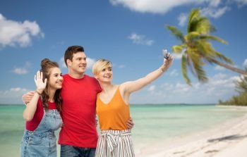 travel, tourism and summer holidays concept - group of happy smiling friends taking selfie by smartphone and hugging over exotic tropical beach with palm trees background. friends taking selfie by smartphone and hugging