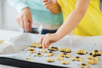 family, cooking and baking concept - mother and little daughter with sprinkles decorating cookies on tray at home kitchen. mother and daughter making cookies at home