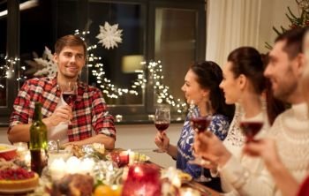 holidays and celebration concept - happy friends with glasses of wine having christmas dinner and speaking toast at home. friends celebrating christmas and speaking toast