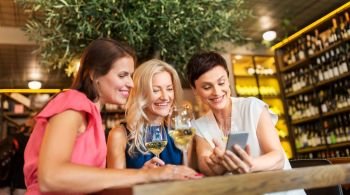 people, technology and lifestyle concept - women with smartphone drinking wine at bar or restaurant. women with smartphone at wine bar or restaurant