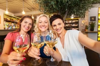 people, technology and lifestyle concept - women drinking wine and taking selfie at bar or restaurant. women taking selfie at wine bar