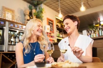 leisure, people and lifestyle concept - happy women eating snacks at wine bar or restaurant. women eating snacks at wine bar or restaurant