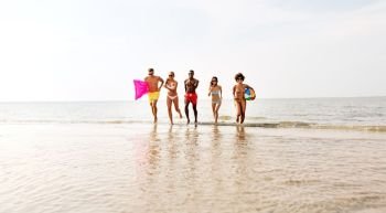 friendship, summer holidays and swimming concept - happy friends with floating mattress and inflatable ball running on beach. friends run with beach ball and swimming mattress