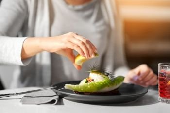 food, new nordic cuisine and people concept - woman eating toast skagen with shrimps, lemon mayonnaise, caviar and buttery bread and squeezing lemon at cafe or restaurant. woman eating caviar salad at cafe or restaurant