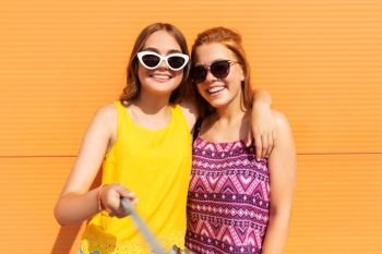 fashion, leisure and people concept - smiling teenage girls taking selfie by monopod outdoors in summer. teenage girls taking selfie outdoors in summer