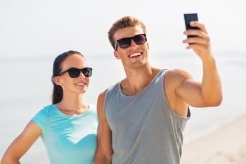fitness, sport and lifestyle concept - happy couple in sports clothes and sunglasses taking selfie by smartphone on beach. couple taking selfie by smartphone on beach