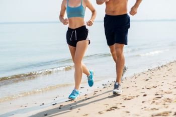 fitness, sport and lifestyle concept - close up of couple running along summer beach. couple in sports clothes running along on beach