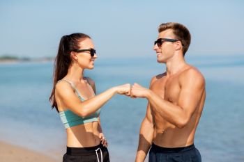 fitness, sport and lifestyle concept - happy couple in sports clothes and sunglasses on beach making fist bump gesture. happy couple in sports clothes and shades on beach