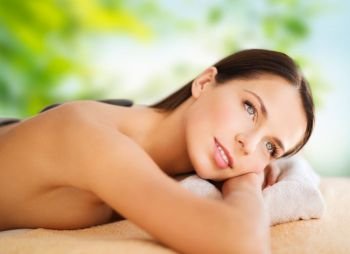 wellness, spa and beauty concept - beautiful woman having hot stone therapy over green natural background. beautiful woman having hot stone therapy at spa
