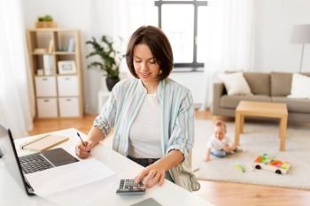 multi-tasking, freelance and motherhood concept - working mother with laptop computer counting on calculator and baby boy playing at home office. working mother counting on calculator and baby