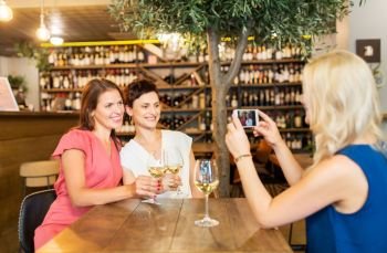 people, technology and lifestyle concept - woman photographing friends drinking wine by smartphone at bar or restaurant. woman picturing friends by smartphone at wine bar