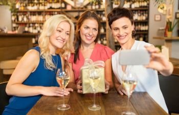 technology, celebration and birthday concept - happy women with gift taking selfie at wine bar or restaurant. women with gift taking selfie at wine bar