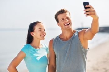 fitness, sport and lifestyle concept - happy couple in sports clothes and sunglasses taking selfie by smartphone on beach. couple taking selfie by smartphone on beach