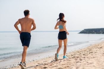 fitness, sport and lifestyle concept - happy couple running along summer beach. couple in sports clothes running along on beach