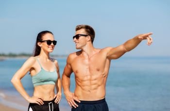 fitness, sport and lifestyle concept - happy couple in sports clothes and sunglasses on beach. happy couple in sports clothes and shades on beach