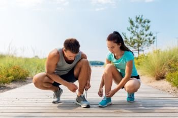 fitness, sport and lifestyle concept - couple of joggers tying sneakers shoelaces outdoors. couple of joggers tying sneakers shoelaces