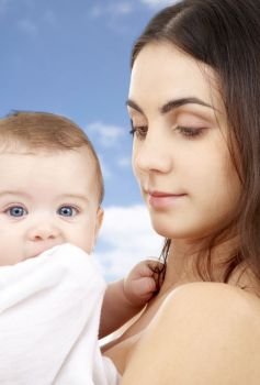 family and motherhood concept - young mother with little baby wrapped into bath towel over sky background. mother with baby in bath towel over sky background