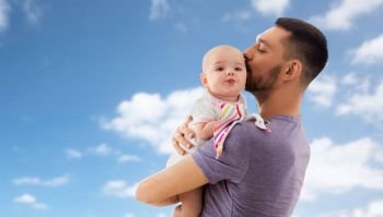 family, parenthood and people concept - happy father kissing little baby daughter over blue sky and clouds background. father kissing little baby daughter